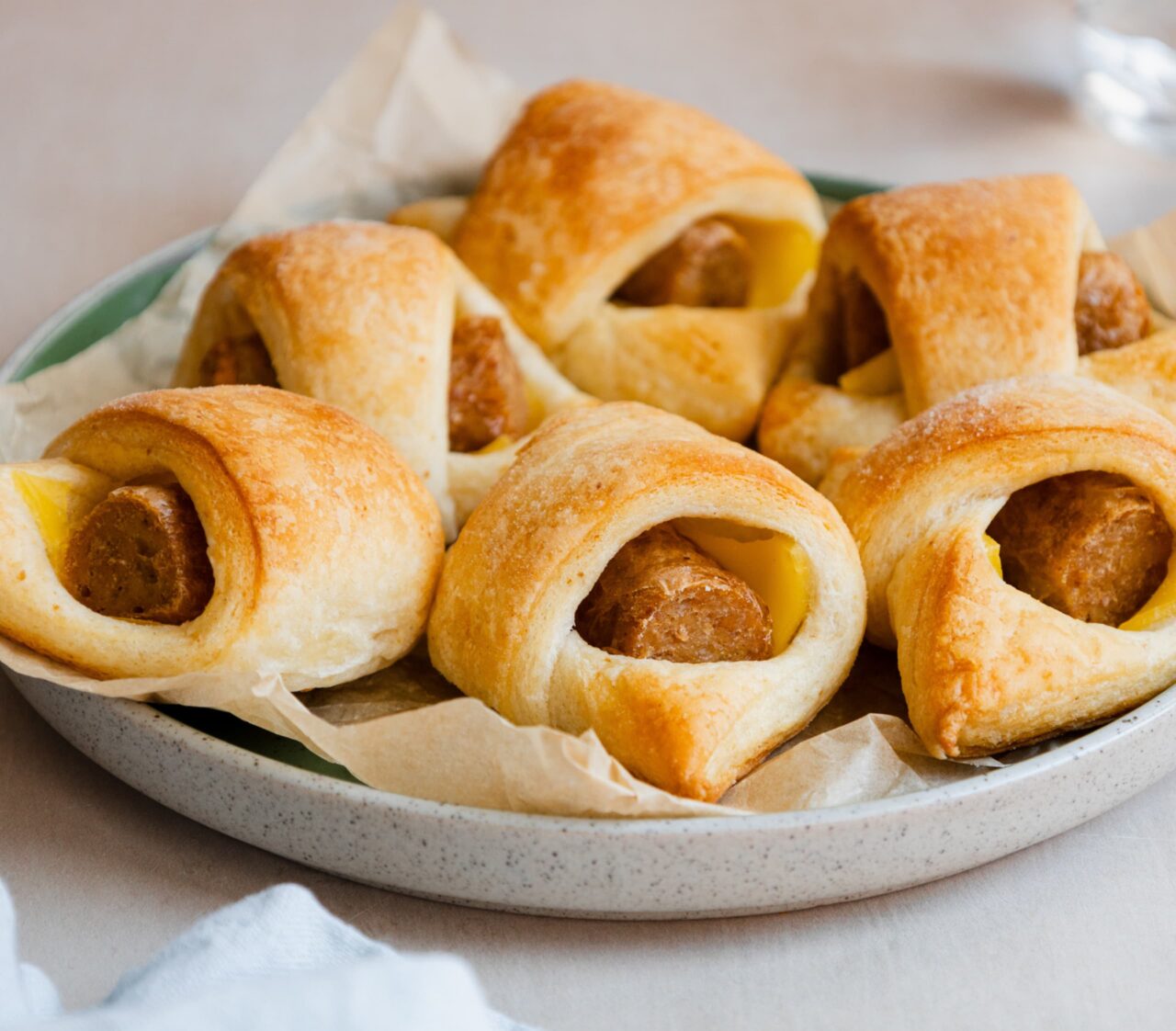 Close-up of Easy Plant-Based Pigs in a Blanket on a green plate, with golden crescent dough wrapped around plant-based hot dogs and melted dairy-free cheese.