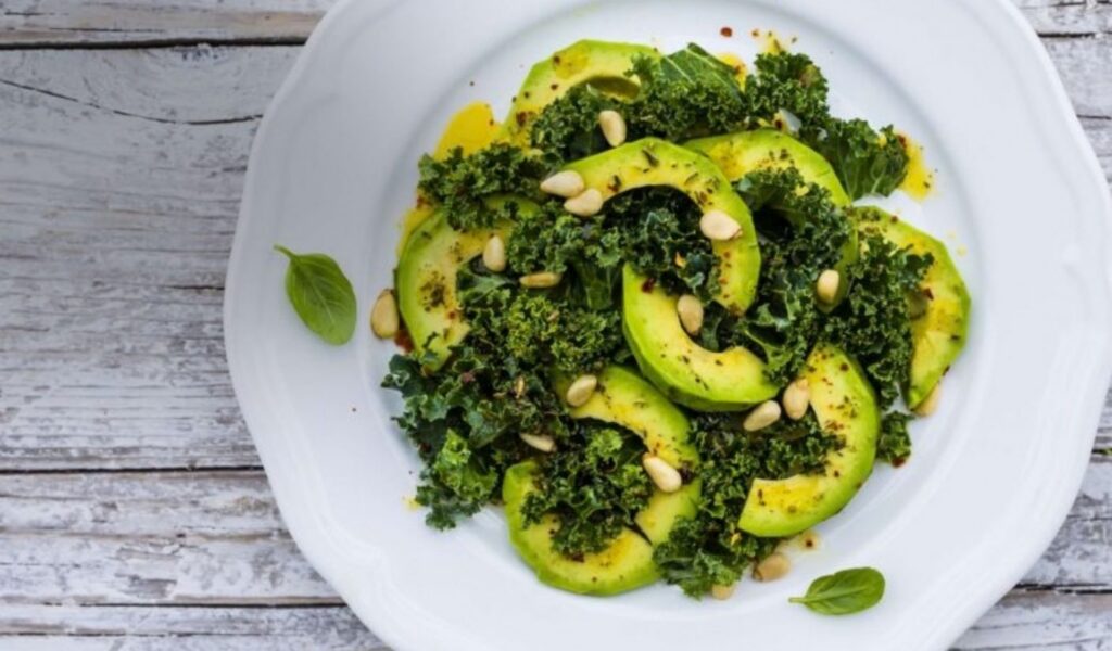 A plate of avocado and kale salad with quinoa, mixed seeds, and a lemon dressing.
