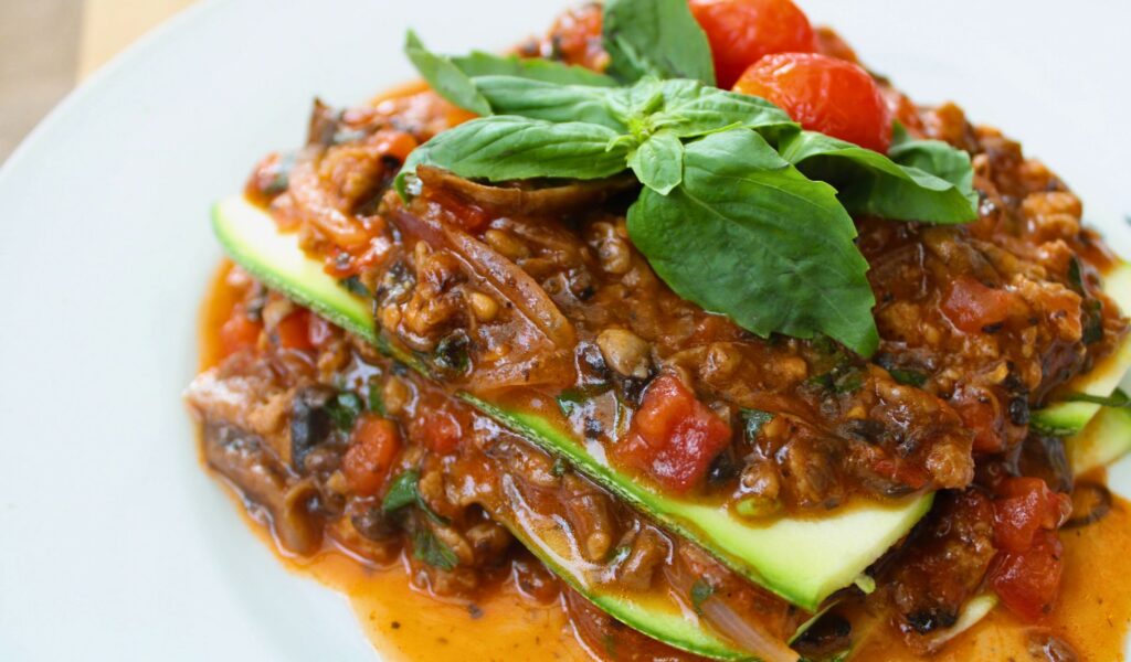 A plate of raw zucchini lasagna layered with tofu, spinach, and tomato pesto.