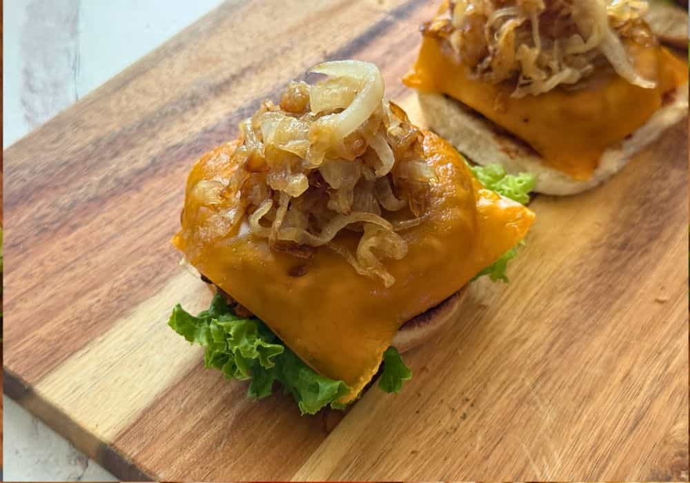 Close-up of an open-faced BBQ black bean cheeseburger with melted cheddar, caramelized onions, and lettuce on a wooden board.