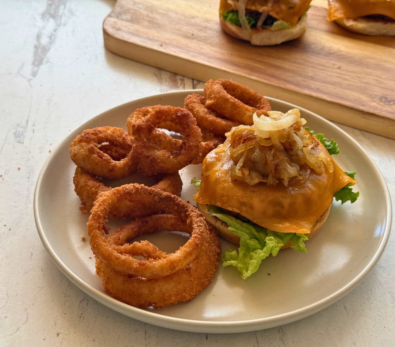 BBQ black bean cheeseburger topped with melted cheddar and caramelized onions on lettuce, served with onion rings on a plate.