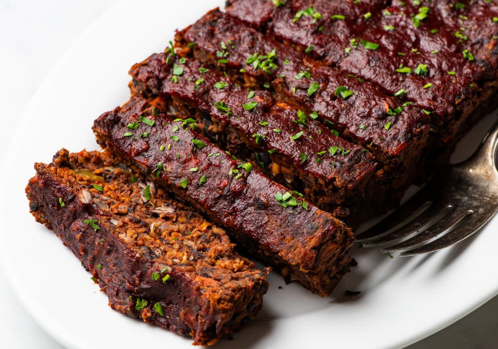 Close-up of black bean meatloaf slices showing a hearty texture with walnuts, oats, and carrots under a glossy balsamic glaze.