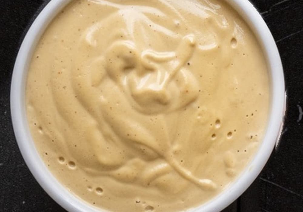 A white bowl of creamy homemade cashew queso on a dark marble surface.
