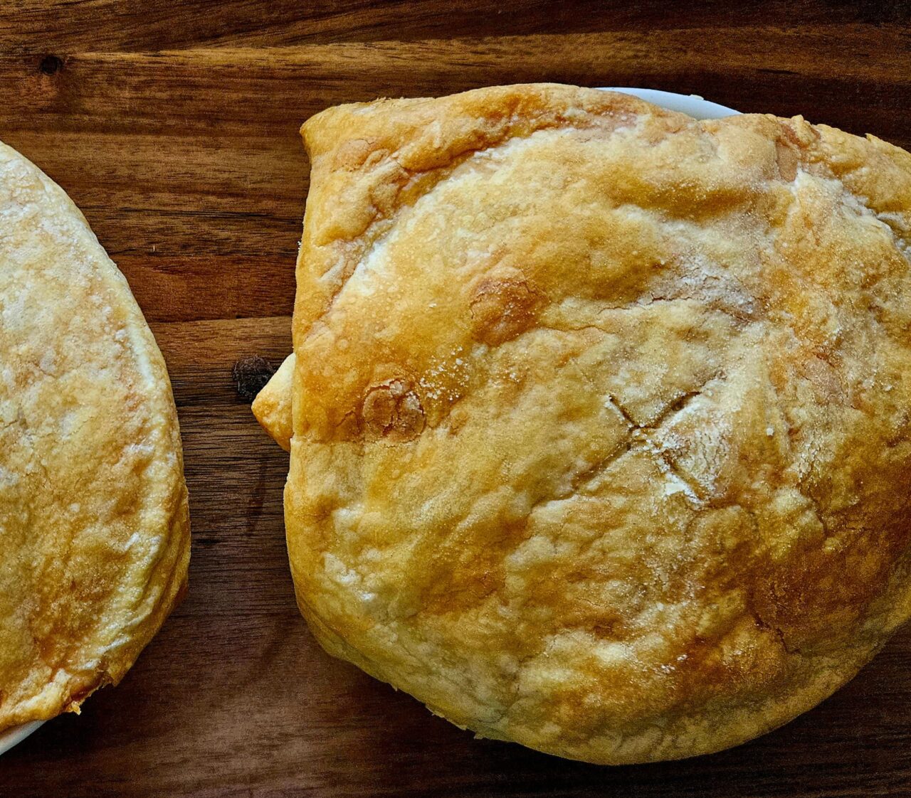Two golden, baked Chickpea Pot Pies with flaky puff pastry tops on a dark wooden board.
