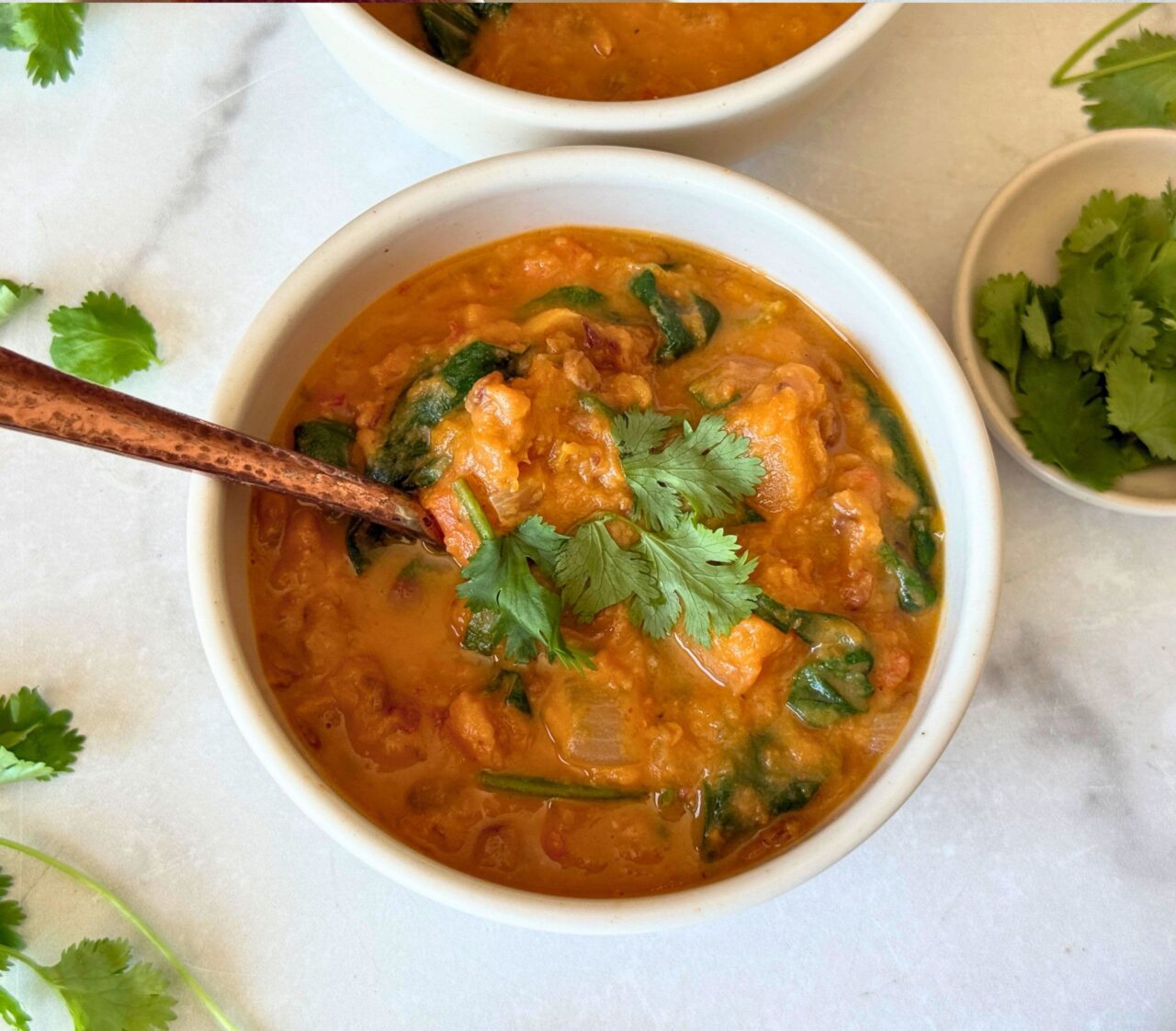 Close-up of a bowl of Coconut Lentil Soup with Butternut Squash and Spinach, garnished with fresh cilantro, with a copper spoon.