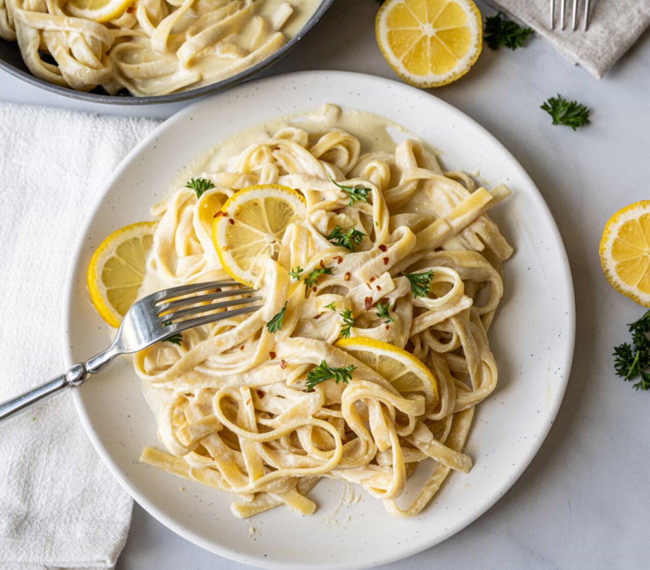 Creamy vegan fettuccine Alfredo with silken tofu, topped with lemon slices, parsley, and red pepper flakes.