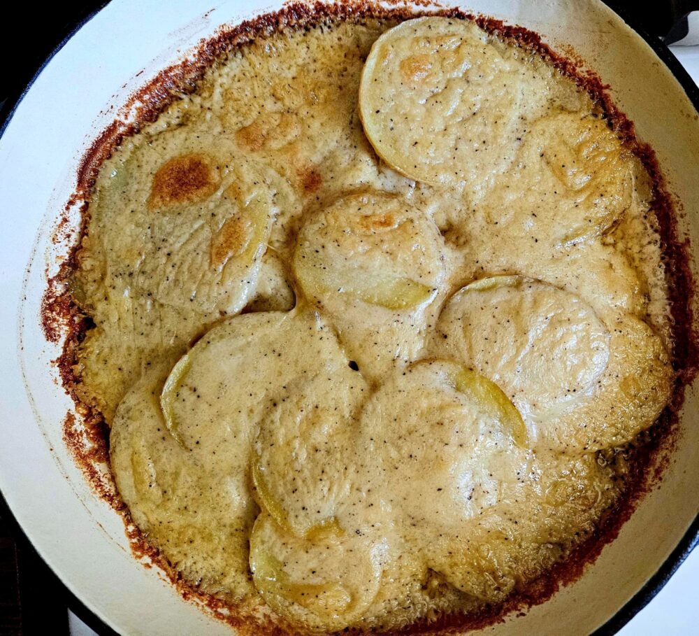 Overhead view of Dairy-Free Scalloped Potatoes in a skillet, with thinly sliced potatoes in a bubbly parmesan sauce and golden browned edges.