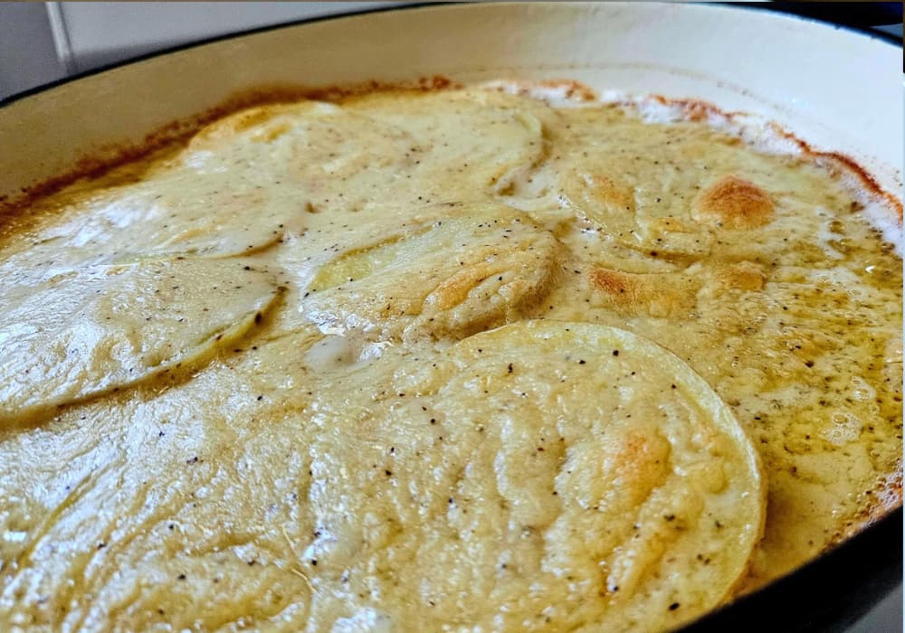 Angled close-up of Dairy-Free Scalloped Potatoes in a skillet, showing layers of tender potato slices in a creamy parmesan sauce with golden spots on top.