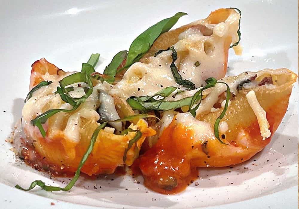 A serving of Garlic and Herb Stuffed Shells on a white plate with marinara sauce, melted dairy-free mozzarella, fresh basil, and cracked black pepper.