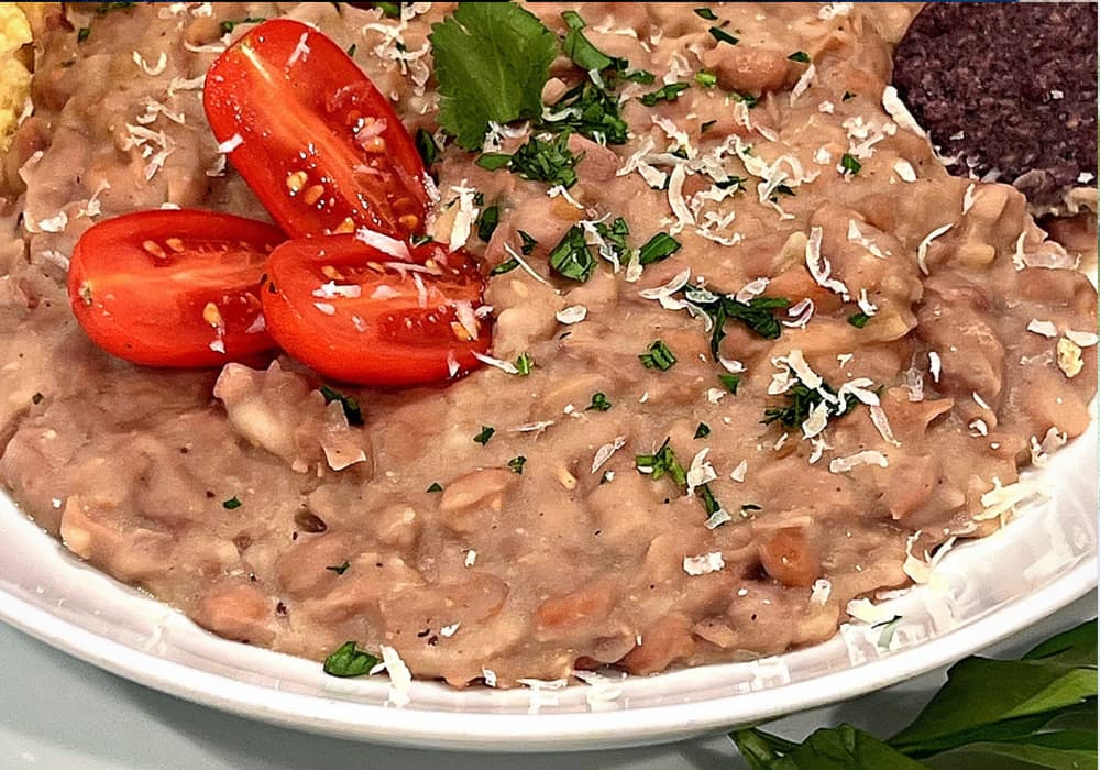 Close-up of creamy Instant Pot Refried Beans topped with grated dairy-free parmesan, chopped cilantro, and halved cherry tomatoes.