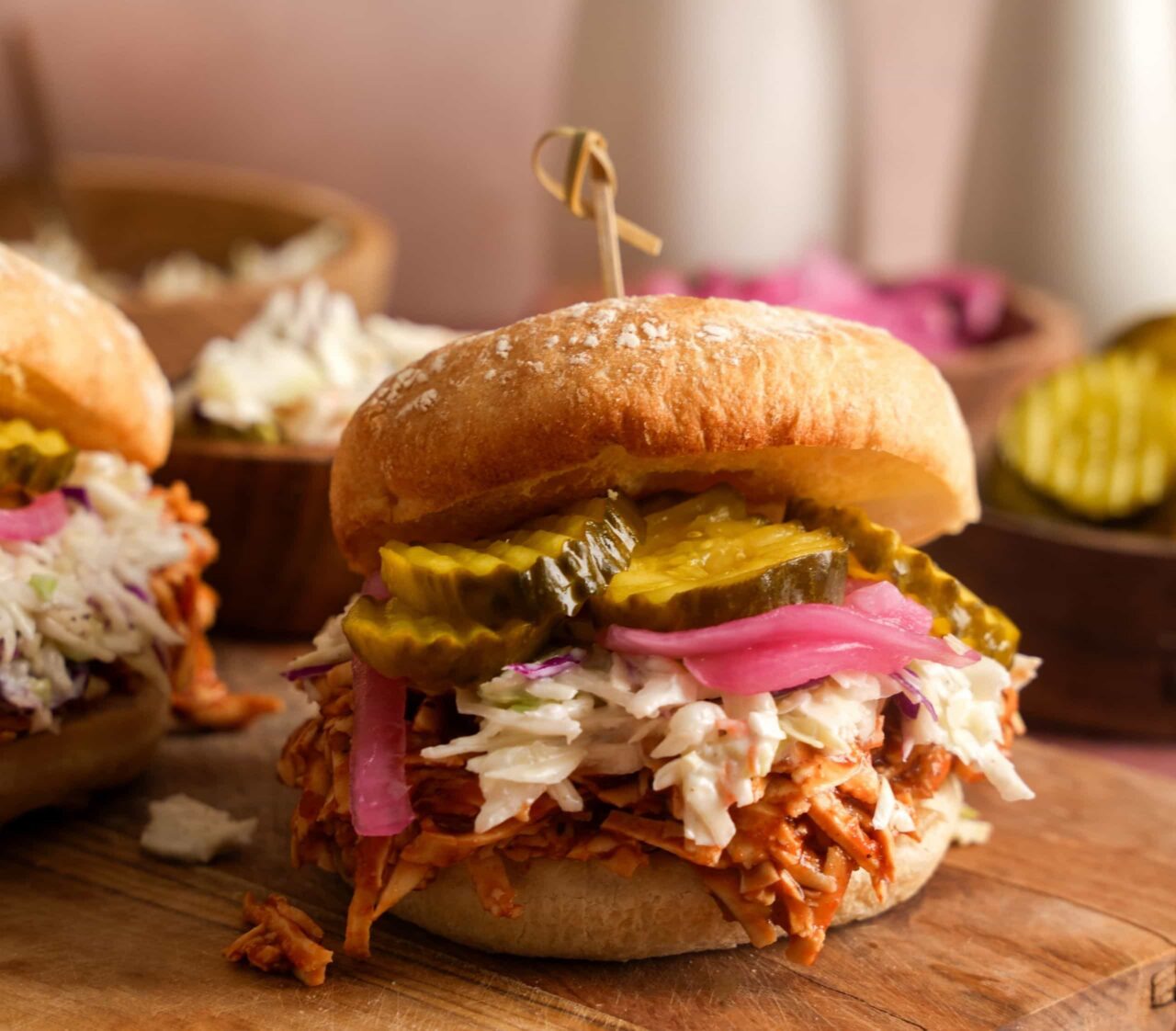 Shredded BBQ tofu sandwich topped with creamy coleslaw, pickled red onions, and dill pickles on a bun.