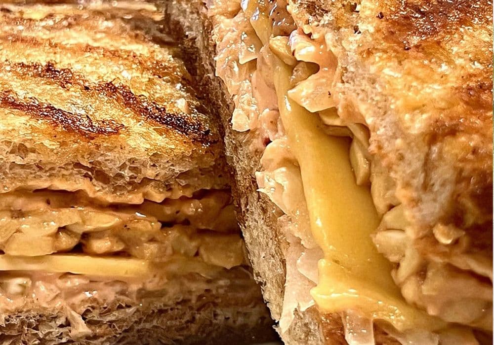 Close-up of a Tempeh Reuben cut in half, showing melted dairy-free provolone, thousand island dressing, and sauerkraut between slices of grilled rye bread.