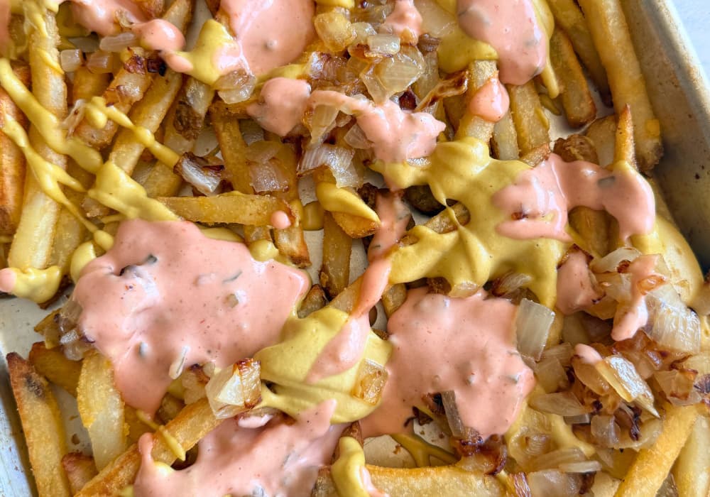 Close-up of crispy fries loaded with creamy cashew cheese sauce, pink special sauce with pickle relish, and browned onions.