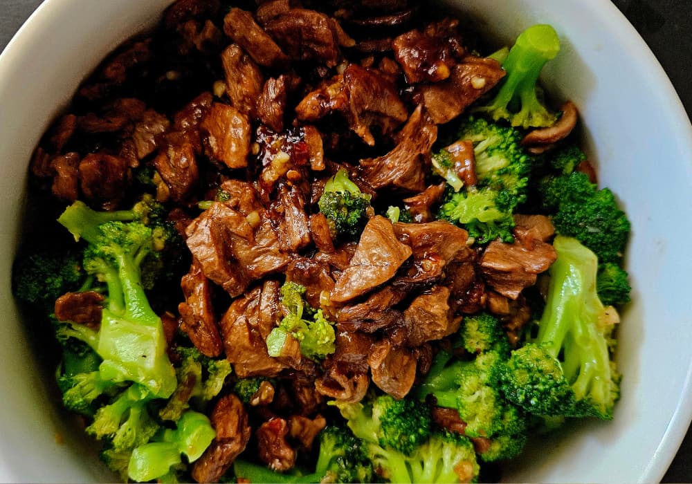 Close-up of Vegan Beef and Broccoli showing glossy plant-based steak bites, garlic, and red pepper flakes tossed with steamed broccoli.